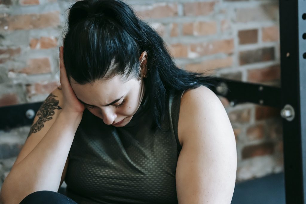 Upset female sitting near sports equipment and feeling desperate and hopeless at training in fitness club